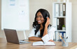 © Prostock-studio - Smiling business woman with headset looking at camera, using laptop for online communication at office