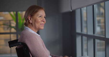 Mature woman sitting in wheelchair in nursing home looking out of window