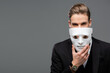 businessman holding mask near face while looking at camera isolated on grey