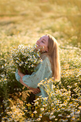 Beautiful girl with long blond hair and a beautiful slack in a chamomile field with a bouquet of flowers on a background of blue sky 