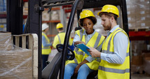 African Female Fork Lift Truck Driver Discussing Checklist With Foreman In Warehouse