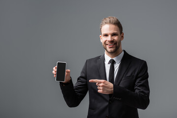 Wall Mural - cheerful businessman pointing at smartphone with blank screen isolated on grey