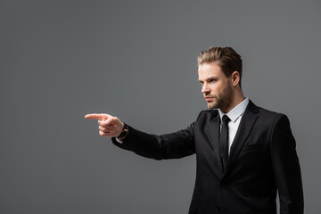 Wall Mural - serious businessman looking away and pointing with finger isolated on grey