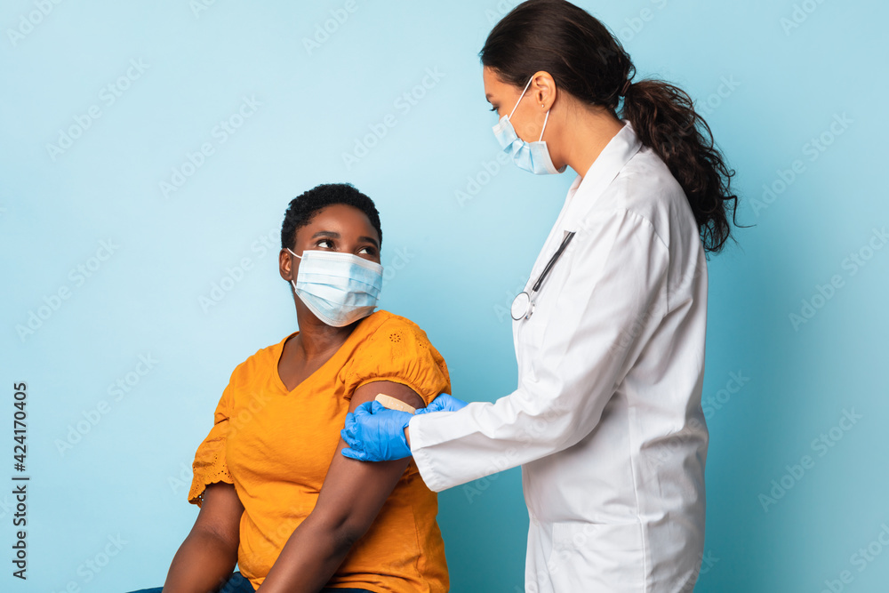 Medical Worker Vaccinating Black Woman Wearing Face Masks, Blue Background - obrazy, fototapety, plakaty 