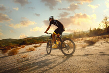 Cyclist Riding A Bike Trough Desert On  Sunset. He Wear Full Equipment For Triathlon.