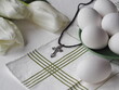 The pectoral cross lies on a white background with eggs and white tulips.Easter background concept with cross.