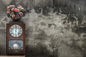 Heart shape wreath made from dried fruits placed over an vintage wood pendulum clock which is leaning against the cement wall. Concept of 