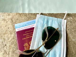 Covid 19 vaccine passport concept  for restrictions on travel with sunglasses, UK passport and covid mask and vaccine ID card by swimming pool