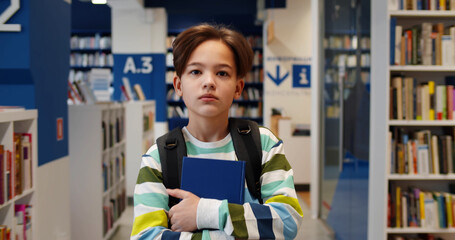 Poster - Portrait of schoolboy with backpack carrying books walking in school library