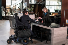 Businessman On Wheelchair At Hotel Reception Desk