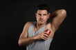 © New Africa - Handsome man applying deodorant to armpit on black background