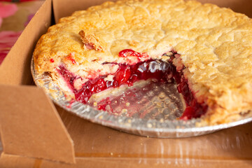 A view of a cherry pie inside a box, featuring a missing piece.