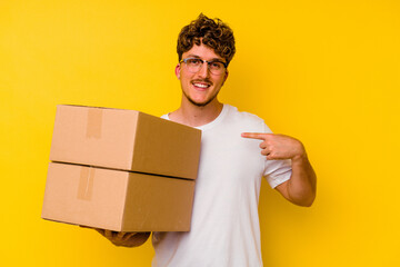 Young caucasian man holding a cardboard box isolated on yellow background person pointing by hand to a shirt copy space, proud and confident