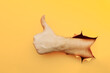 © burdun - Hand showing a thumb up sign through a ripped hole in yellow paper wall. Well done, good job concept