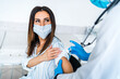 © Тарас Нагирняк - Beautiful smiling woman in a protective mask during vaccination against coronavirus, the doctor injects the vaccine into his hand. Safe vaccination against covid 19