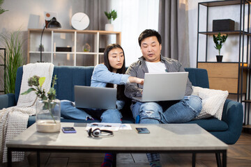 Group of two young people using personal laptops while doing homework. Asian students sitting on couch together and studying. Concept of technology and education.