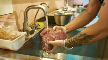  Close up of hands of male cook cleaning the raw pork under tap water for cooking