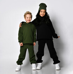 Studio full-length portrait of little european boy and preteen asian girl children model wearing warm trendy sportswear posing for camera isolated on white copy space. Kids fashion