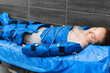 A young girl lies on a couch with closed eyes in a pressotherapy suit and lymphatic drainage therapy.