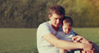 © guas - Portrait close up of happy young father and son child together sitting on a grass in a park
