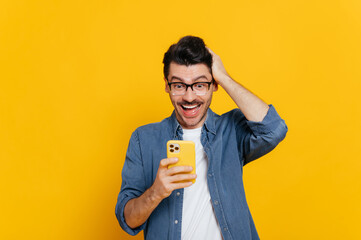 cheerful excited modern positive caucasian guy uses his smartphone, texting with friends, browsing i