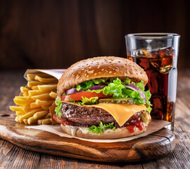 Delicious burger with cola and potato fries on a wooden table with a dark brown background behind. Fast food concept.