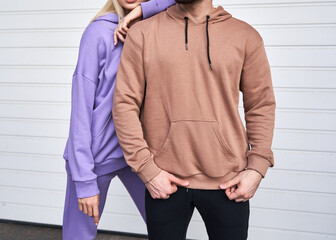 Wall Mural - Blonde girl is standing in blue sport outfit. Man wears brown hoodie and black pants. Couple is wearing street matching outfit