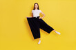 Happy woman after weight loss posing on one hand isolated over yellow background, wearing white casual t shirt and too big black pants, keeps one hand on hip, rejoices at achieved result.