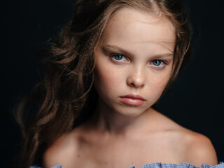 A beautiful blue-eyed girl with bare shoulders on a dark background and curly hair