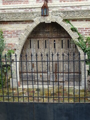 Wall Mural - metal gate and old wooden arch door entrance on a white stone and red brick wall