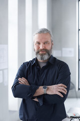 Wall Mural - Portrait of mature bearded businessman smiling at camera while standing with his arms crossed at office