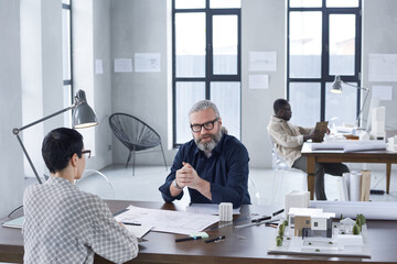 Wall Mural - Group of engineers sitting at the table at meeting and working with blueprints at modern office