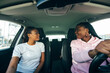 © F8  \ Suport Ukraine - Two african woman friends talking each other in the car while driving car on the city street road