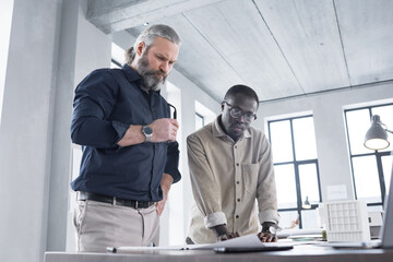 Wall Mural - Two architects working in team standing near the table with blueprints and examining them at office