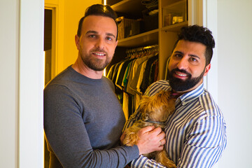 gay couple at the entrance of the dressing room after changing clothes looking at each other in love. One of them has a dog in his hands.