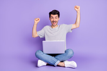 Wall Mural - Photo of guy sit floor hold computer raise fists open mouth wear white t-shirt jeans sneakers isolated violet background