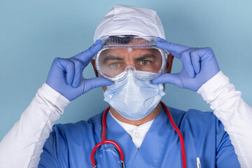 Portrait of Doctor wearing protective mask, medical glasses and a stethoscope. Isolated image on a blue background.