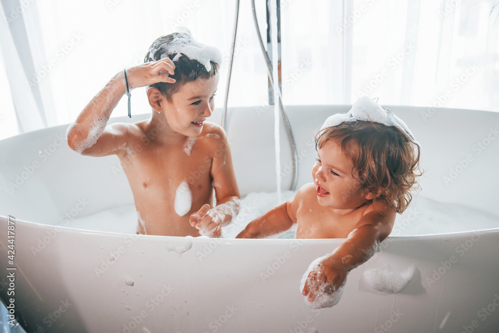 Two kids having fun and washing themselves in the bath at home - obrazy, fototapety, plakaty 
