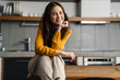 © Drobot Dean - Young brunette woman smiling at camera while sitting on table in kitchen