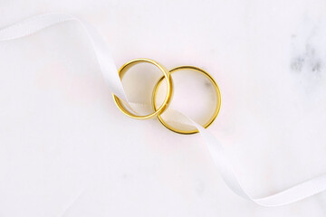 Two golden wedding rings close up with ribbon on white background. Wedding invitation card concept. 