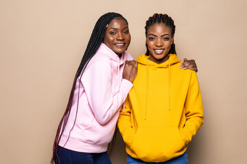 Portrait of two african women hugging and laughing isolated over beige background