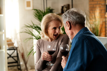 Wall Mural - Senior woman and man drinking wine at home. Husband and wife celebrate the anniversary..