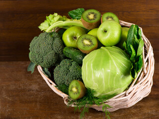 Canvas Print - Green vegetables - kiwi, cabbage, herbs, celery, broccoli, cucumbers in a basket a wooden background