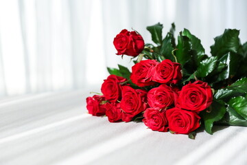 a bouquet of red roses on a table with a white tablecloth with sun glare 