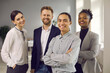 © Studio Romantic - Portrait of young male business leader or executive with team of employees smiling at camera. Happy ethnic man in striped shirt standing arms folded in office with cheerful coworkers in background