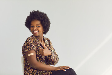 vaccinated young smiling african american woman with medical patch on hand showing thumbs up gesture