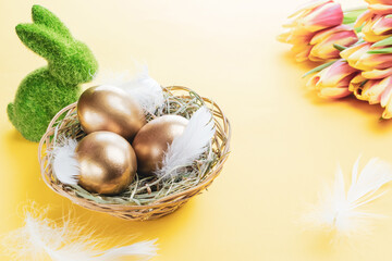 Wall Mural - Easter Golden eggs in basket with spring tulips, white feathers on pastel yellow background in Happy Easter decoration. Spring holiday concept.