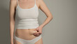 © transurfer - Skinny fat figured unrecognizable woman pinching her belly fat. Woman`s hips closeup raw studio shot in grey background. Dieting and fat loss concept.