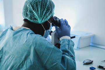 african medical worker in hazmat suit working with microscope inside lab hospital during coronavirus