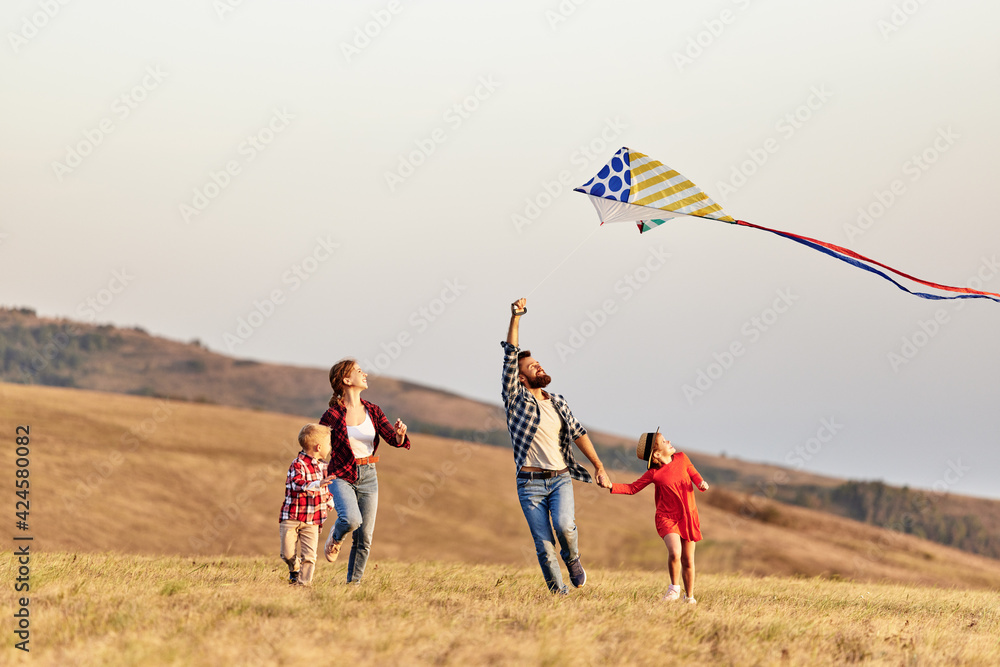 Happy family father,  mother and children launch  kite on nature at sunset - obrazy, fototapety, plakaty 